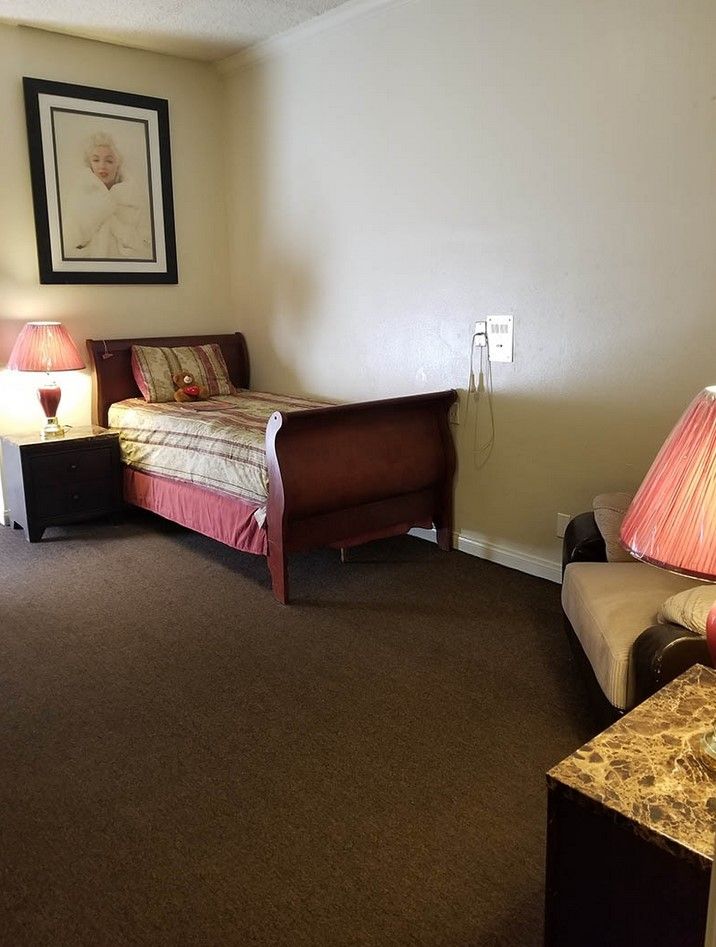 A cozy bedroom with a single bed, nightstand, and lamps providing warm lighting.