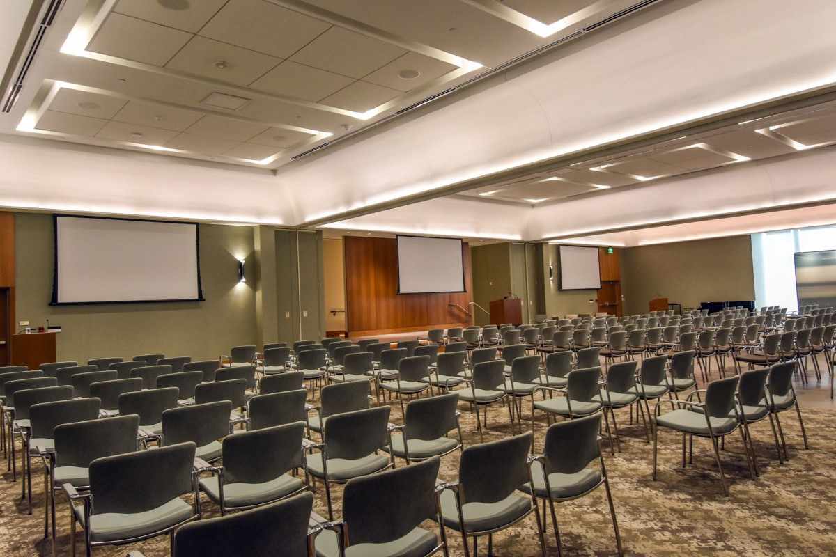 An empty conference room with rows of chairs and projector screens.