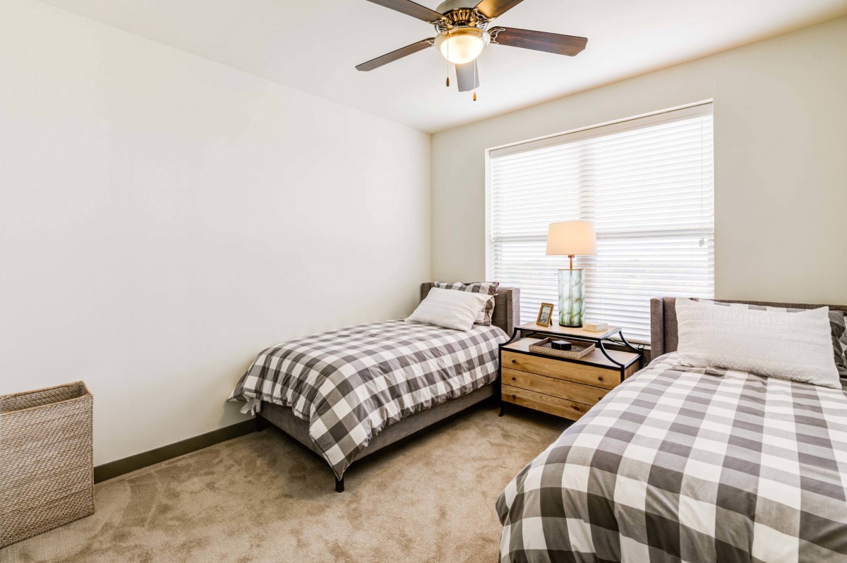 A cozy bedroom with twin beds featuring checkered bedding, a ceiling fan, and a window letting in natural light.