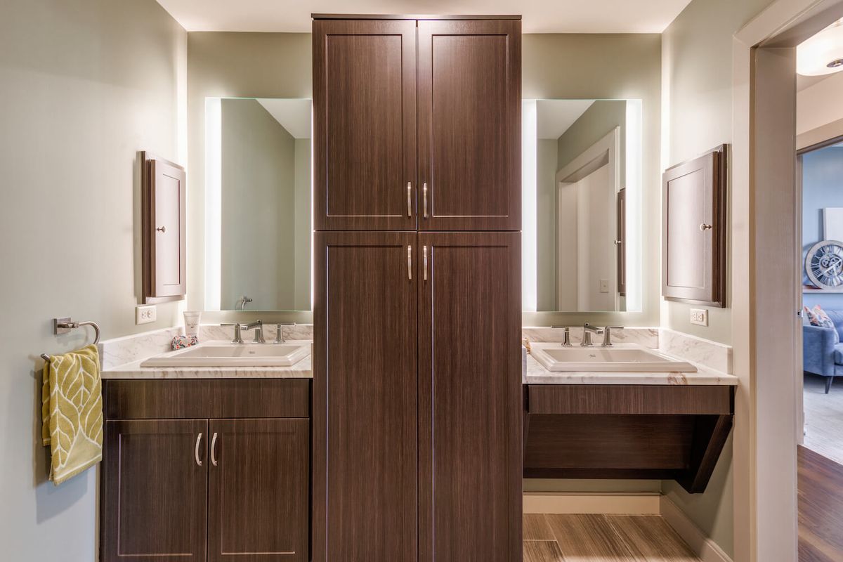 A bathroom with a double vanity featuring two sinks and mirrors, separated by a tall wooden cabinet.