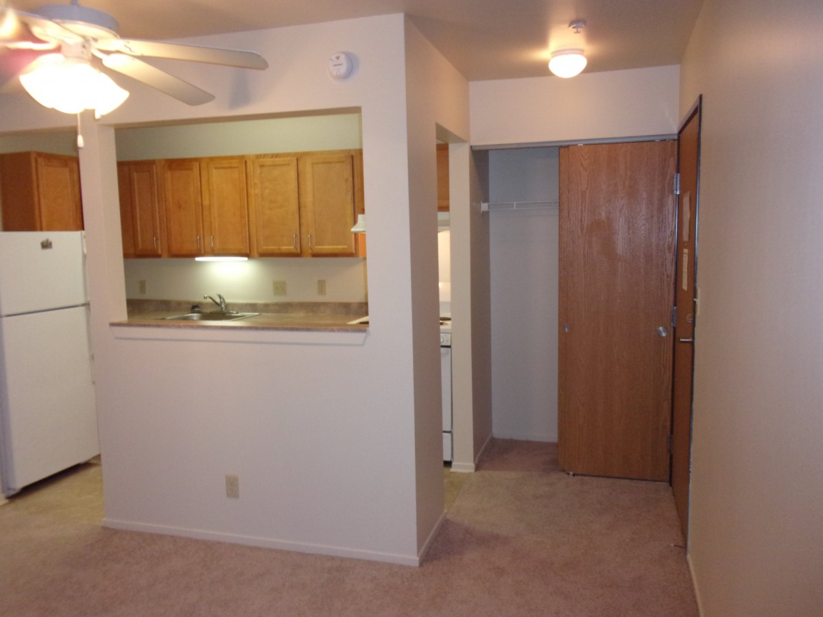 An apartment interior showing a small kitchen and hallway with warm lighting.