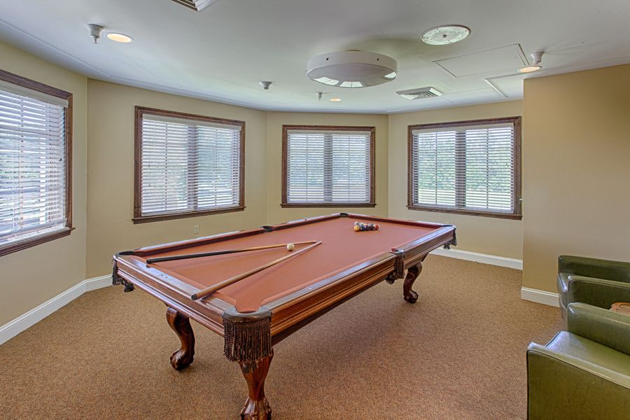 A well-lit game room featuring a classic pool table with cue sticks.