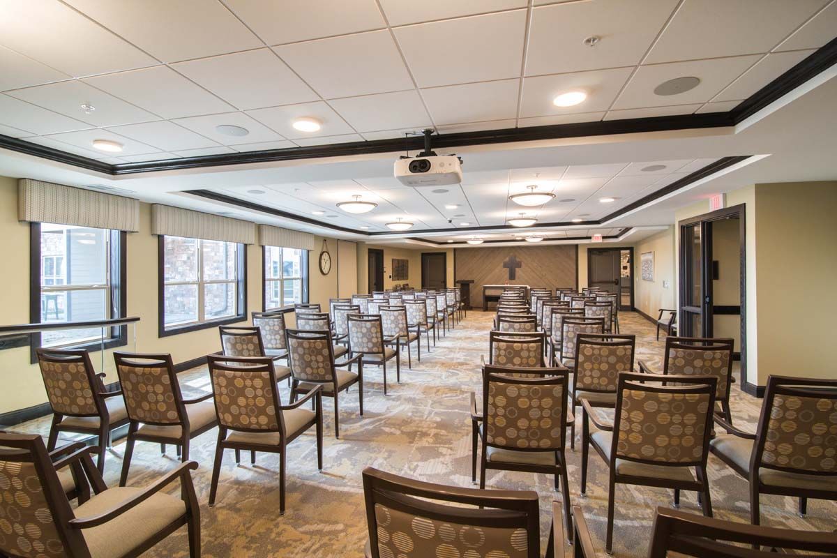 A well-lit conference room set up with rows of chairs and a ceiling-mounted projector.