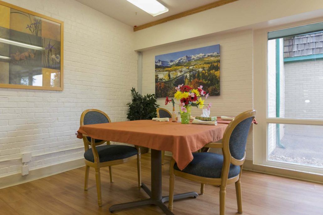 A cozy dining room with a table set for two, adorned with a bouquet of flowers and surrounded by comfortable chairs.