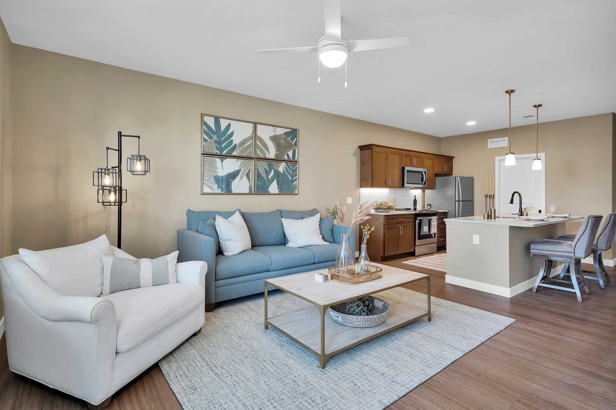 A modern living room with an open kitchen, featuring a blue sofa and a white armchair, accented by stylish decor.
