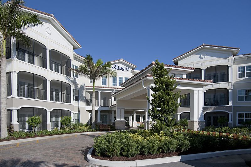 A modern residential building complex with palm trees and landscaped entrance.