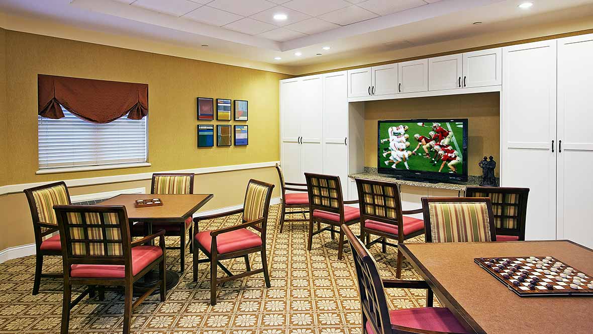 A meeting room with several chairs and tables, featuring a television displaying a sports game.