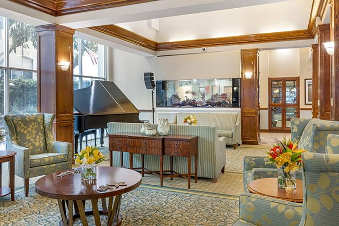 A cozy lounge area featuring elegant furniture, a grand piano, and a large aquarium.