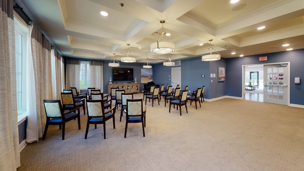 A neatly arranged conference room with chairs facing a television, featuring blue walls and stylish chandeliers.