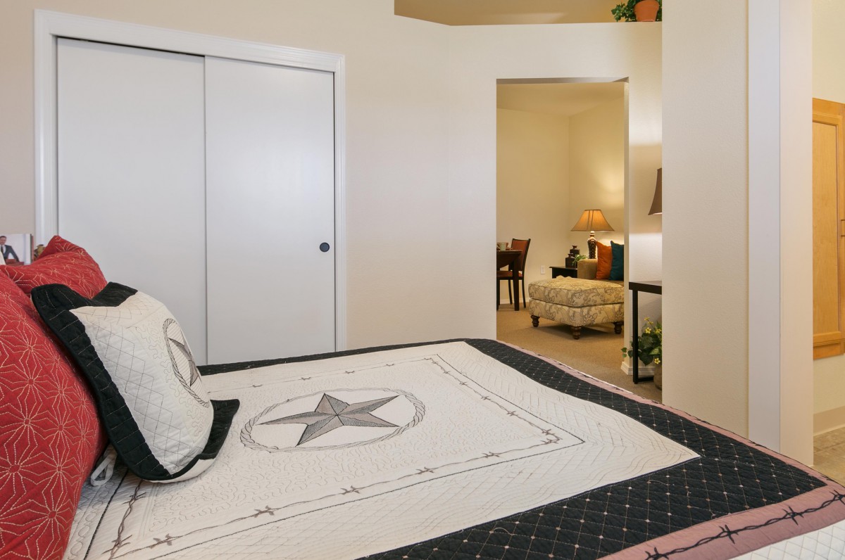 A cozy and minimalist bedroom with neatly arranged bedding and a view into an adjoining room.