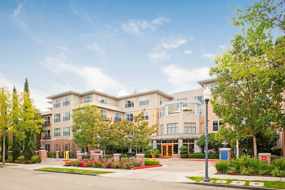 A modern apartment building surrounded by trees under a clear blue sky.