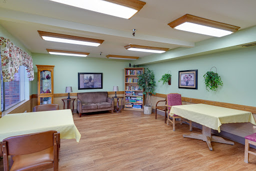 A cozy indoor space featuring comfortable seating, tables, and a bookshelf, illuminated by natural light.
