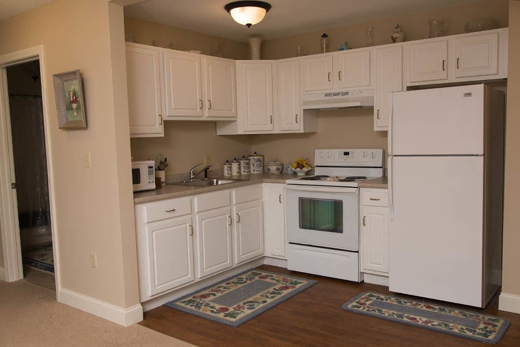 A cozy kitchen with white cabinets, a stove, refrigerator, and microwave.