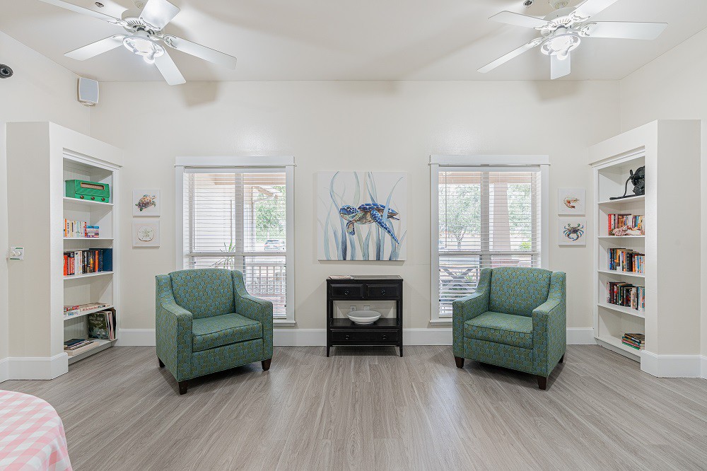 A minimalist living room with two green chairs, large windows, and abstract artwork.