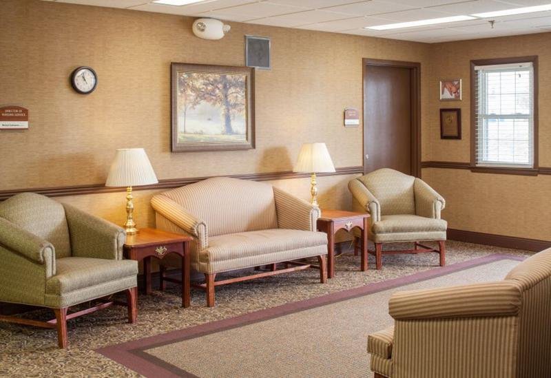 A calm waiting room featuring comfortable seating, side tables with lamps, and a framed painting on the wall.