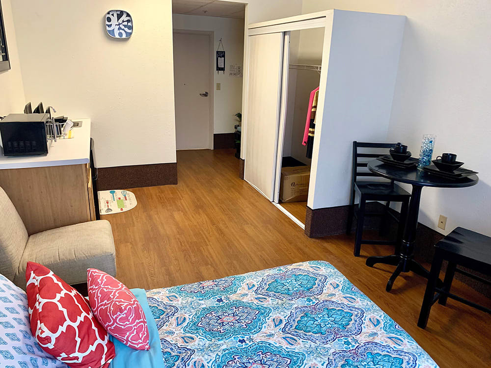 A cozy bedroom with a neatly made bed, small dining setup, and a mirrored closet.
