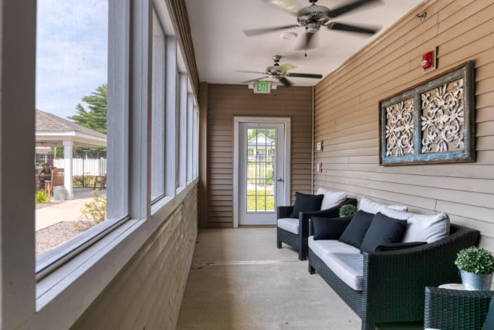 A cozy sunroom with cushioned seating and ceiling fans, offering a view of the outdoors.