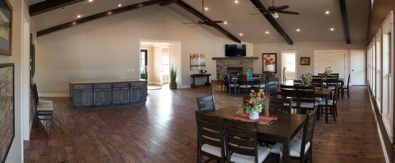 A spacious living room with an open floor plan featuring a dining area, wooden flooring, and vaulted ceilings with exposed beams. The room includes a fireplace and television, creating a cozy atmosphere.