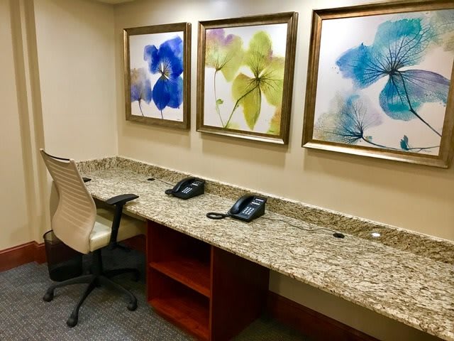 A neatly arranged office space with a granite desk, featuring two telephones and abstract floral artwork on the wall.