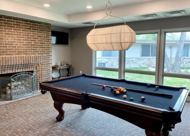 A cozy game room featuring a pool table, brick fireplace, and large windows.