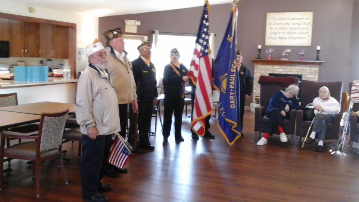 A group of veterans standing in an indoor setting, participating in a flag ceremony with American flags.
