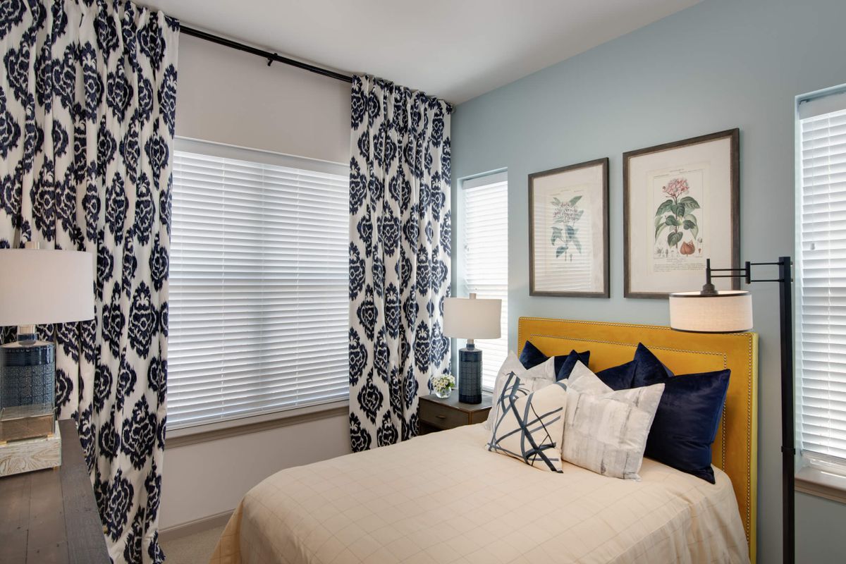 A well-decorated bedroom with patterned curtains, artwork on the wall, and a neatly made bed.