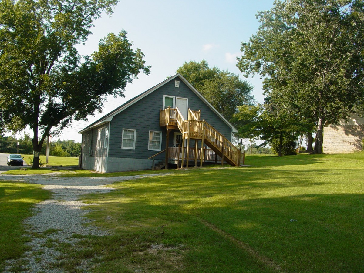 A gray house with a wooden staircase surrounded by trees and grass.