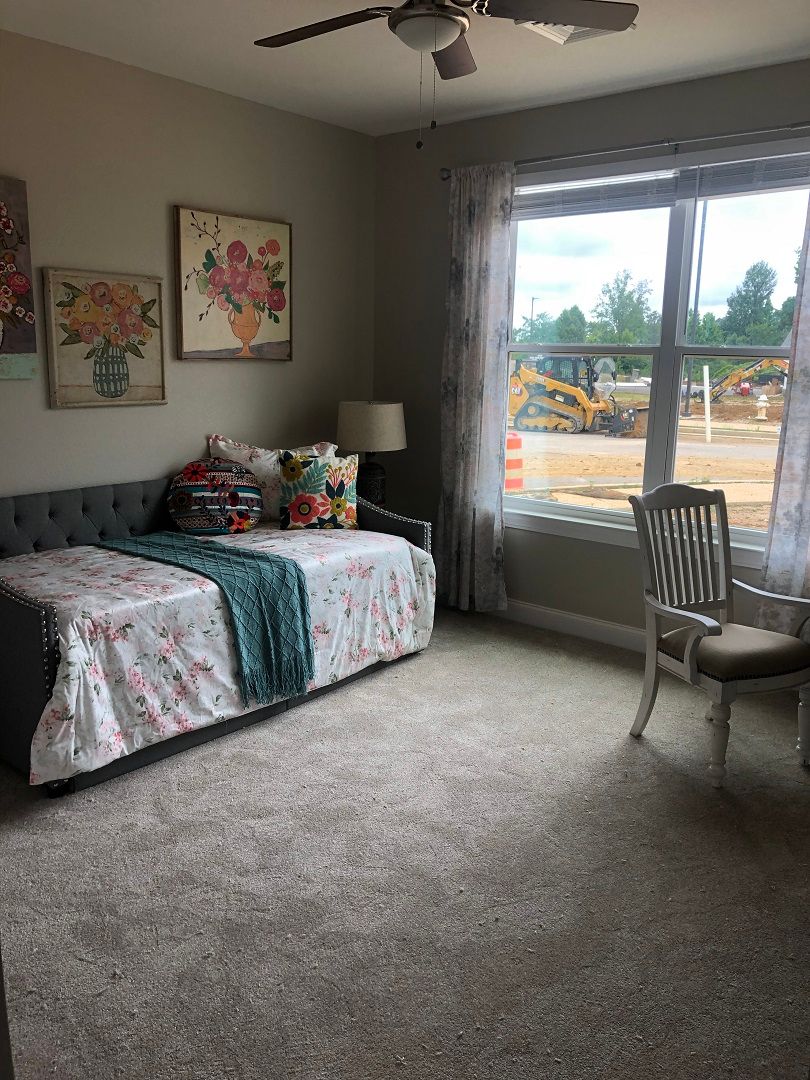 A cozy bedroom with a single bed, floral decor, and a large window overlooking construction.
