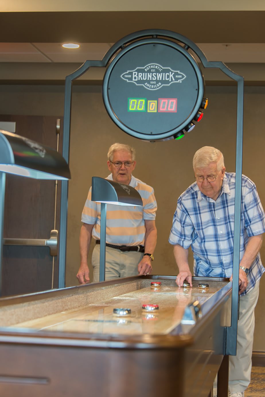 Two seniors enjoying a game of shuffleboard indoors.