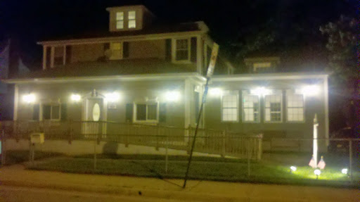 A house illuminated by soft lights at night, with a utility pole leaning precariously nearby.