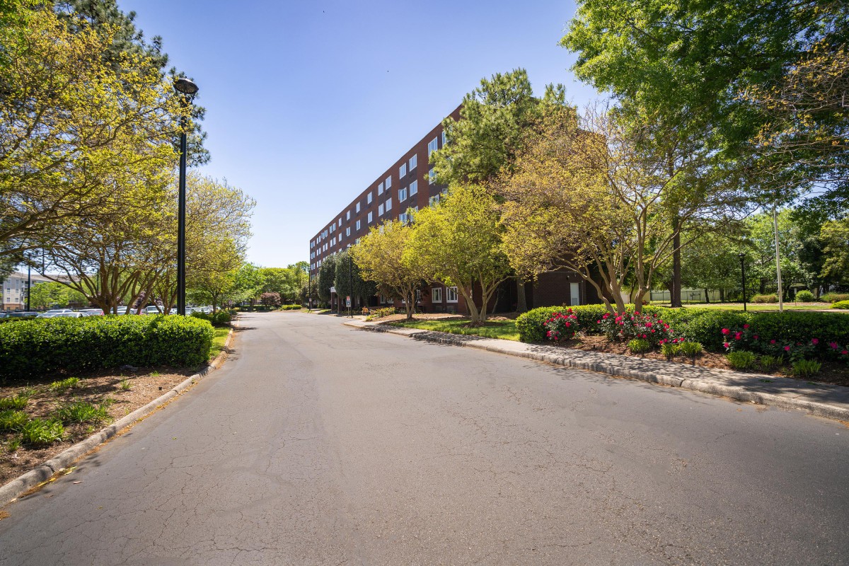 A road alongside a multi-story building surrounded by trees and greenery.
