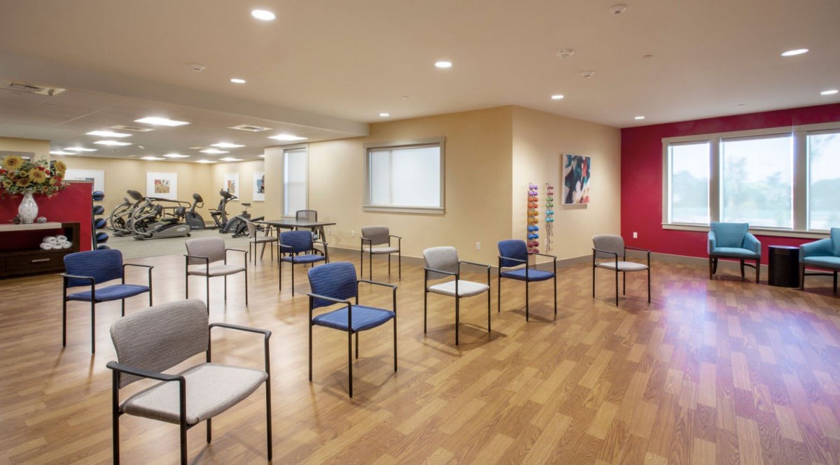 A spacious exercise room with chairs arranged in a circle, featuring wooden flooring and minimalist decor.