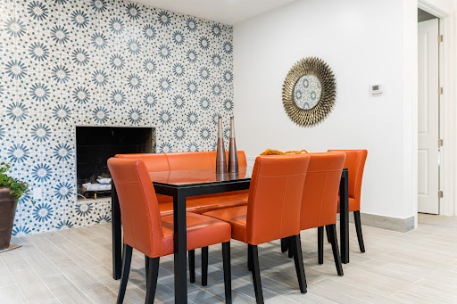 A stylish dining room featuring vibrant orange chairs and a black table, complemented by a decorative wall and contemporary decor.
