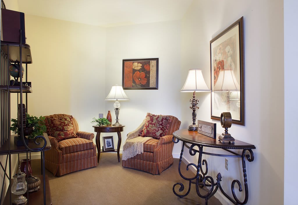 A cozy living room corner with two chairs, a small table, lamps, and decorative artwork.