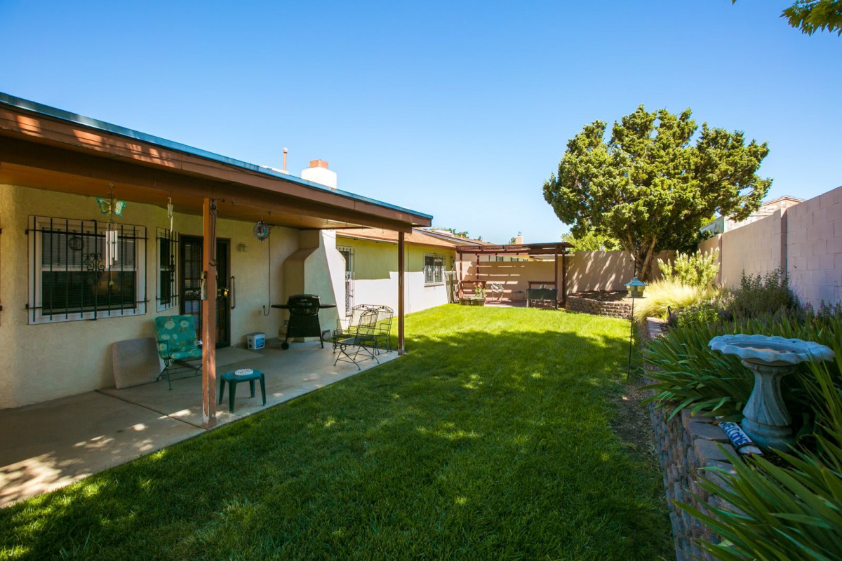 A cozy backyard with a grassy lawn, patio, and outdoor seating under a clear blue sky.