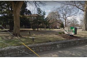 A serene park setting bordered by a stone wall, featuring trees and grass, with a construction trailer in the background.