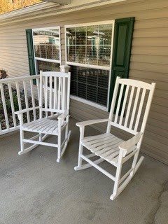 Two white rocking chairs on a porch.