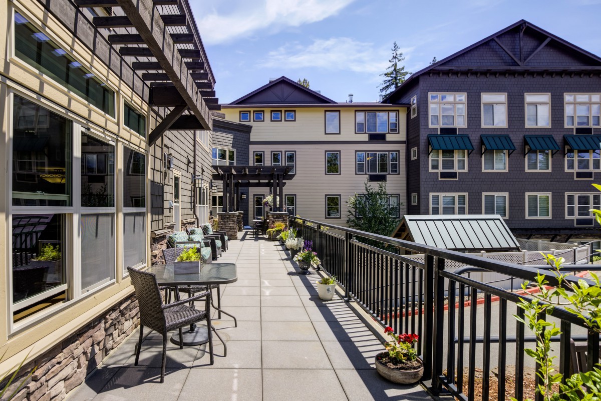 A modern apartment complex with a spacious balcony featuring outdoor seating and plants, under a clear blue sky.
