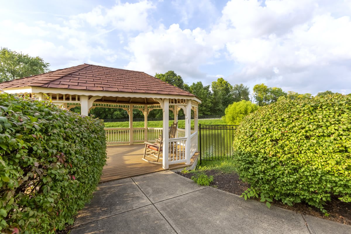 A serene gazebo overlooking a pond in a park setting, surrounded by lush greenery.