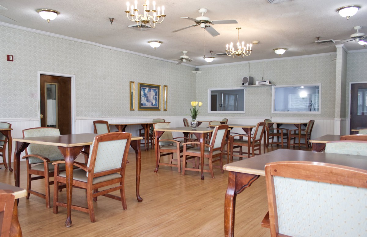 A spacious dining area featuring wooden tables and chairs, adorned with chandeliers and ceiling fans.