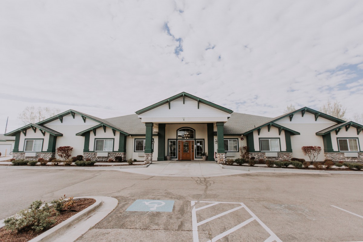 A front view of a single-story building with a parking area in the foreground under a cloudy sky.