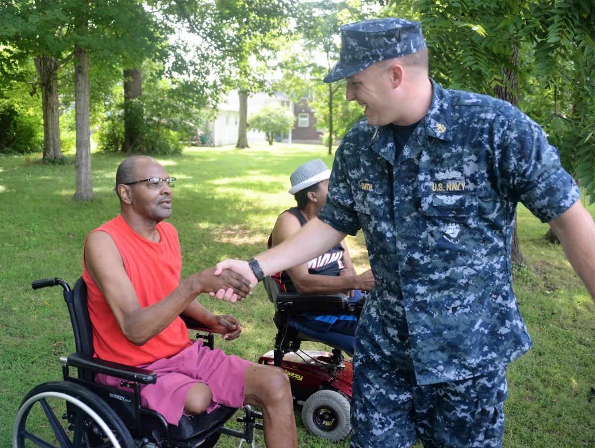 A military personnel shaking hands with a person in a wheelchair outdoors.