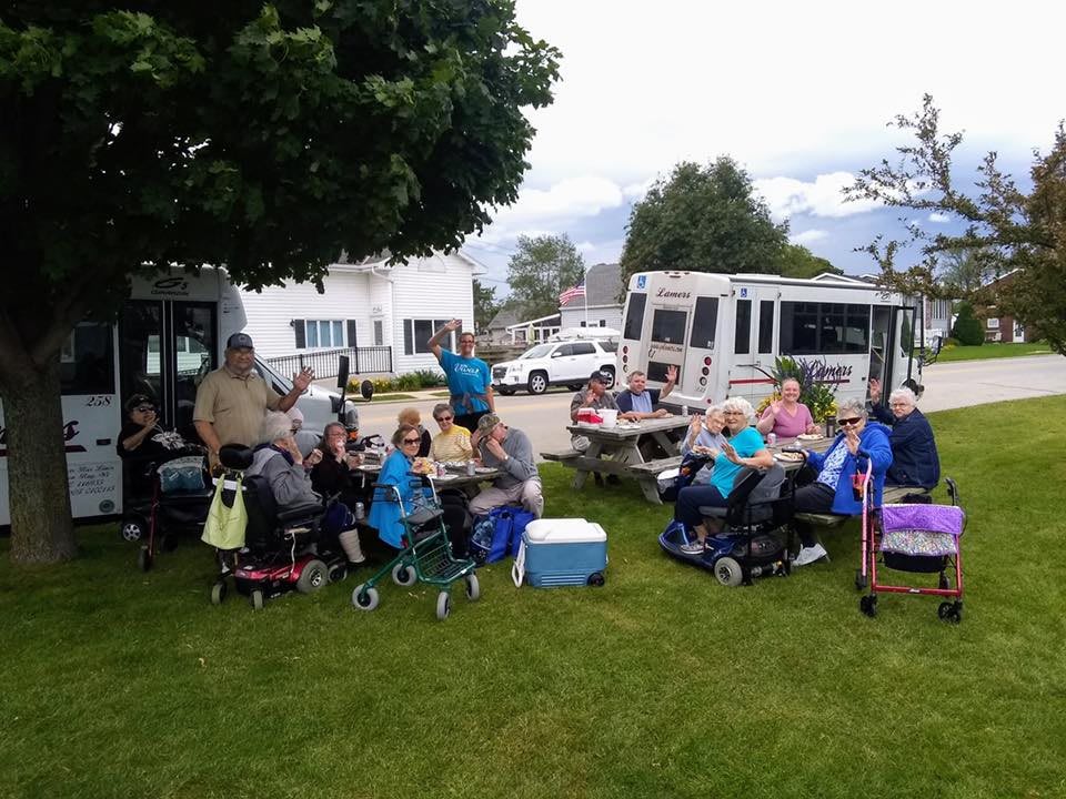 A group of elderly people enjoying an outdoor picnic with buses parked nearby.
