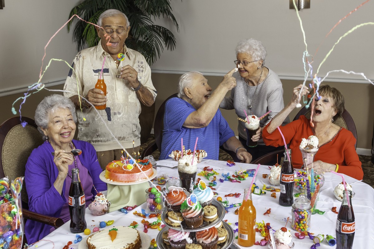 A group of seniors enjoying a lively party with cake, drinks, and laughter.