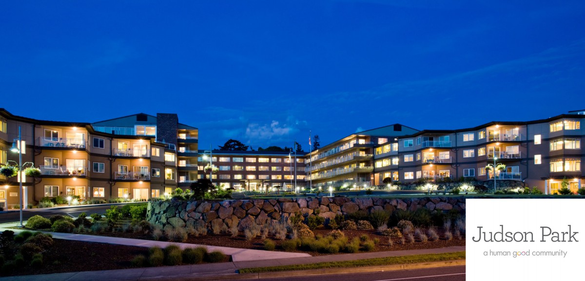 Modern building illuminated at night with landscaped surroundings.