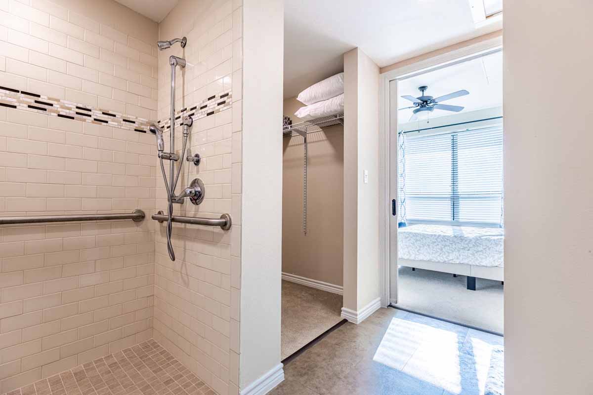 A modern bathroom with a walk-in shower featuring handrails, and neatly stacked towels.