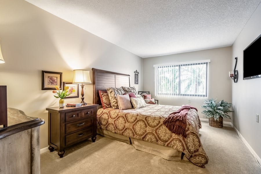 A cozy bedroom with a well-decorated bed, nightstand, and a window letting in natural light.