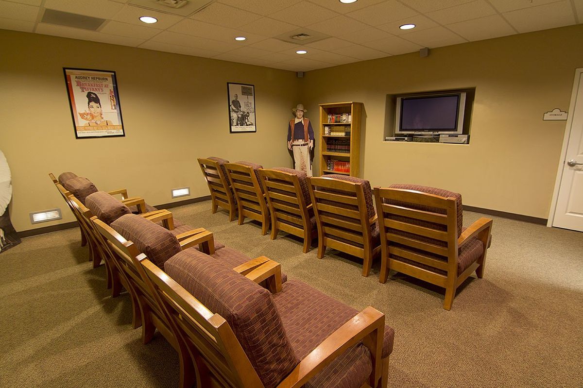 A waiting room with rows of wooden chairs arranged in front of a television.