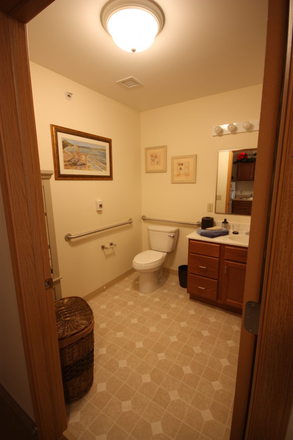 A cozy bathroom featuring a toilet, sink with a mirror, and decorated with artwork and grab bars.