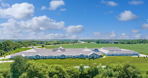 Aerial view of a large building surrounded by lush green fields and a bright blue sky.